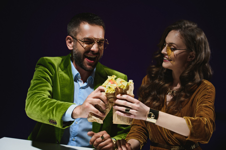 portrait of smiling couple in luxury velvet clothing with shawarma sitting at table with dark background behindの写真素材