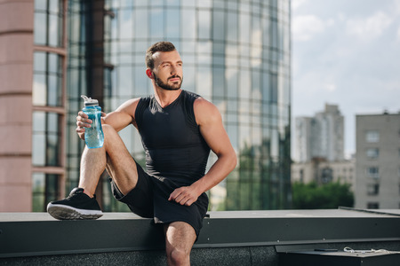 handsome sportsman resting and holding sport bottle of water on roofの写真素材