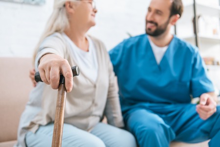 close-up view of senior woman holding walking cane and looking at smiling male nurseの写真素材