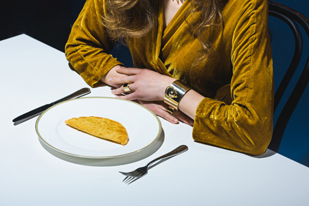 partial view of woman in luxury clothing sitting at table with meat cheburek on plate with blue backdropの写真素材