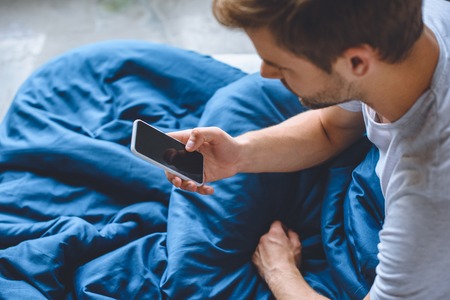 selective focus of young man in bed using smartphone with blank screenの写真素材