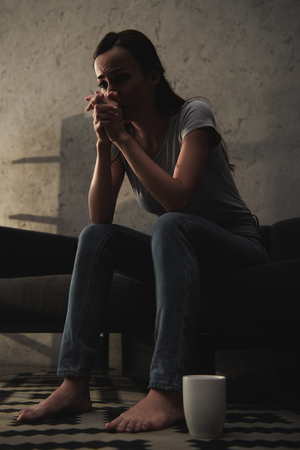 bottom view of crying woman sitting on sofa with coffee cup on floorの写真素材
