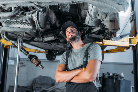 professional workman with crossed arms looking at car in mechanic shop