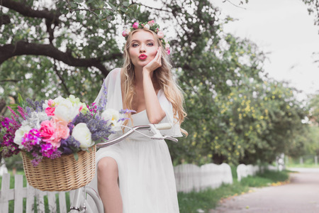 beautiful young bride riding bicycle with flower basket and looking at cameraの写真素材