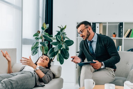 patient lying on sofa and talking to therapist in officeの写真素材