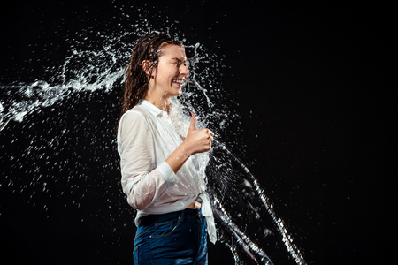 side view of smiling woman in white shirt showing thumb up while swilled with water isolated on blackの写真素材