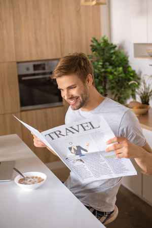 smiling man reading travel newspaper at kitchen table with breakfastの写真素材
