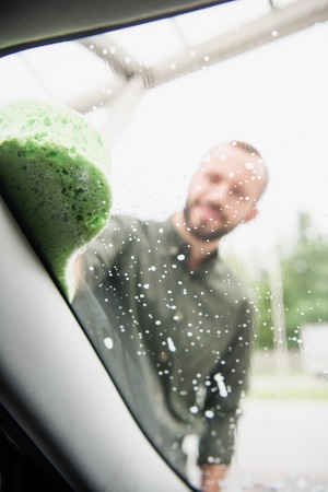 selective focus of man cleaning car front window with rag and soap at car washの写真素材