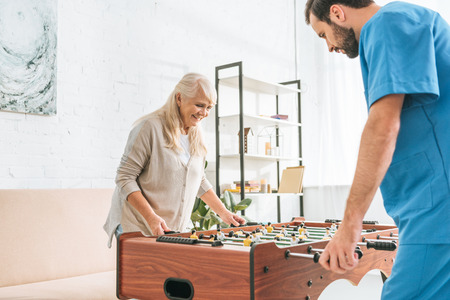 smiling senior woman and young social worker playing table football togetherの写真素材