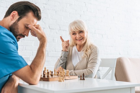 smiling senior woman pointing with finger and looking at upset man after chess gameの写真素材
