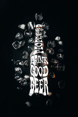 flat lay with glass bottle of beer on ice cubes arranged on dark tabletop with "good people drink good beer" inspirationの写真素材