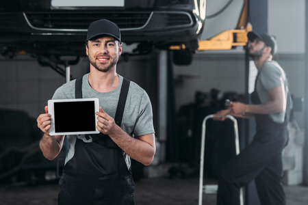 auto mechanic holding digital tablet with blank screen, while colleague working in workshop behindの写真素材
