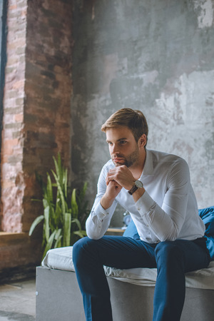 thoughtful businessman sitting on bed in bedroom at homeの写真素材
