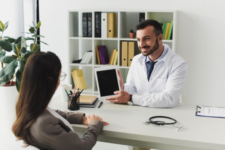 smiling doctor showing patient gadget with blank screen in clinicの写真素材