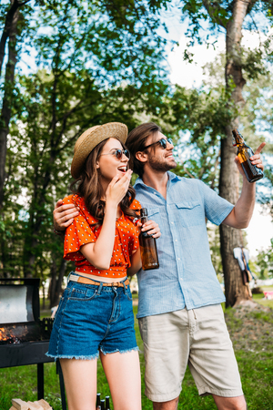 cheerful couple in sunglasses with beer looking away in parkの写真素材