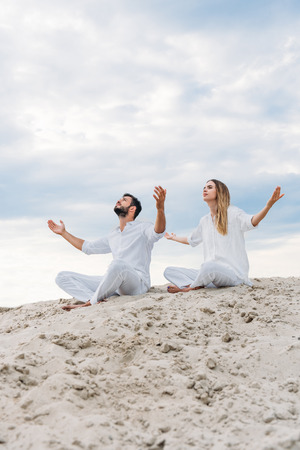 young fit couple on yogi meditating while sitting on sandy dune in lotus pose (padmasana)の写真素材