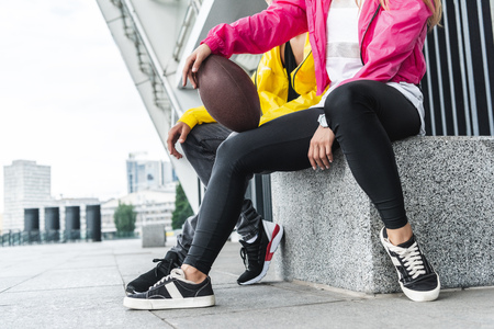 cropped image of young smiling couple sitting rugby ball at urban cityの写真素材