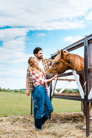 couple of happy ranchers palming horse in stableの写真素材