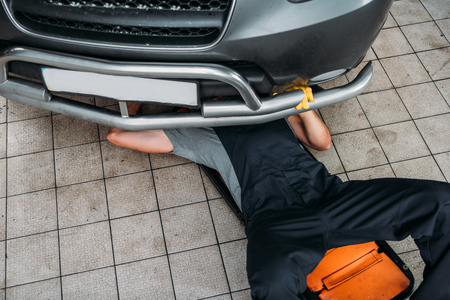 high angle view of workman lying and working under car in mechanic shopの写真素材