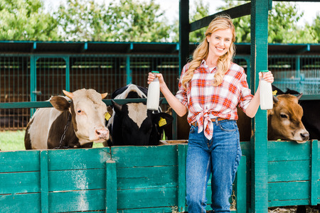 beautiful farmer showing bottles of cow milk near stableの写真素材