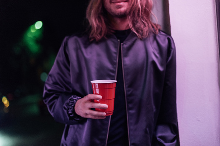 cropped shot of young man with red plastic cup of drink on street at night under pink light