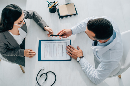 high angle view of doctor giving pen to patient to sign insurance claim form in clinicの写真素材