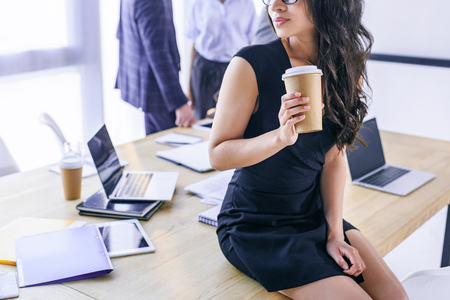 partial view of african american businesswoman with coffee to go and colleagues behind in officeの写真素材