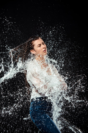 side view of woman in white shirt and jeans swilled with water isolated on blackの写真素材