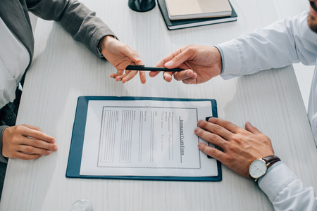 cropped image of doctor giving pen to patient to sign insurance claim form in clinicの写真素材