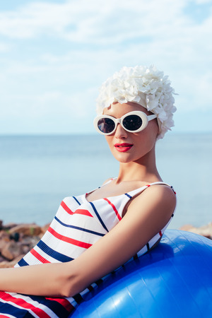 young woman in striped swimsuit, sunglasses and white hat relaxing on fit ballの写真素材