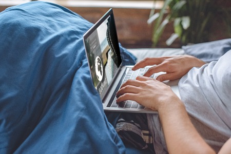 cropped image of man in bed using laptop with booking website on screen