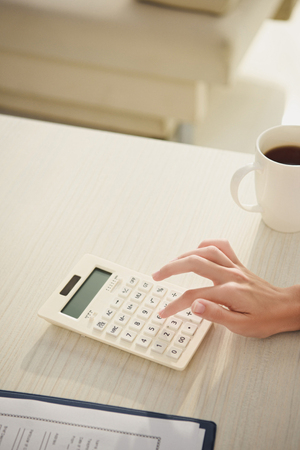 cropped view of woman counting finances on calculator at table with cup of coffeeの写真素材