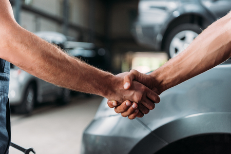 cropped view of mechanics shaking hands in auto repair shopの写真素材