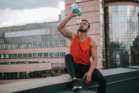 handsome sportsman pouring water from bottle on face on roofの写真素材