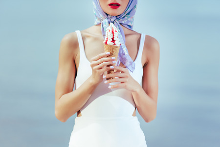 cropped view of girl in vintage white swimwear and silk scarf holding ice cream in waffle coneの写真素材
