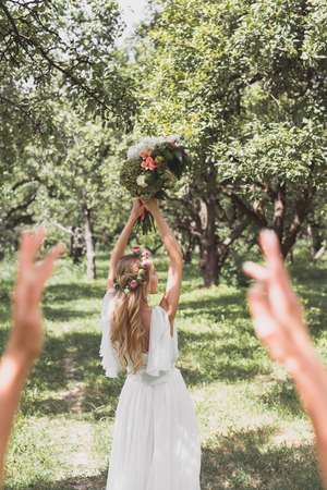 selective focus of young bride throwing wedding bouquet in parkの写真素材