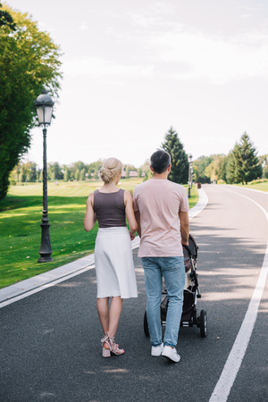 rear view of parents walking with baby carriage on road in parkの写真素材