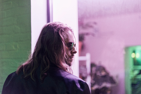 rear view of young man in leather jacket and sunglasses looking away on street at night under pink lightの写真素材