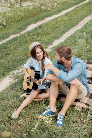 smiling woman playing acoustic guitar to boyfriend in summer filedの写真素材