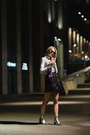 stylish young woman with mojito in plastic cup on dark streetの写真素材