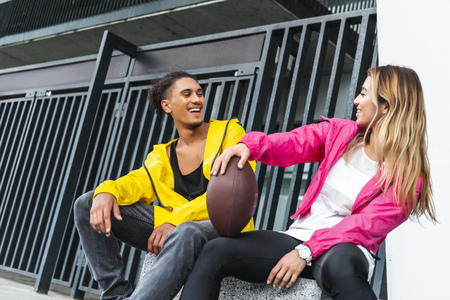 young smiling multicultural couple sitting rugby ball at urban cityの写真素材