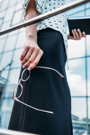 partial view of businesswoman with eyeglasses and notebook in hands standing on streetの写真素材