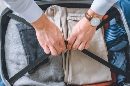 cropped image of businessman with wristwatch packing luggage in suitcaseの写真素材