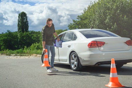 handsome man holding car insurance and putting traffic cones on roadの写真素材