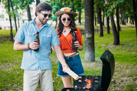 smiling couple in sunglasses with beer setting fire on grill togetherの写真素材