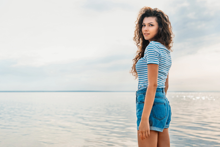 attractive curly girl in casual clothes posing near the seasの写真素材