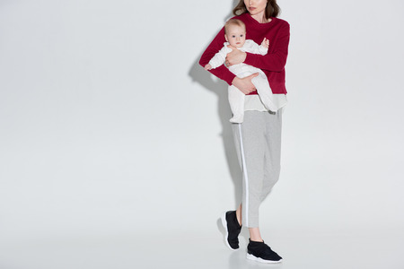 cropped shot of stylish mother carrying adorable baby girl on greyの写真素材