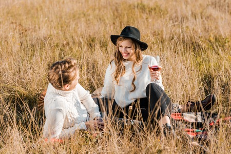 smiling couple holding wineglasses and looking at each other during picnic on meadowの写真素材