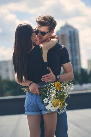 sexy multiethnic couple embracing and holding bouquet of flowers on roofの写真素材