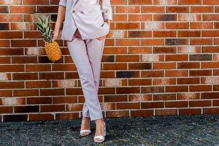 cropped shot of stylish woman with pineapple standing in front of brick wall